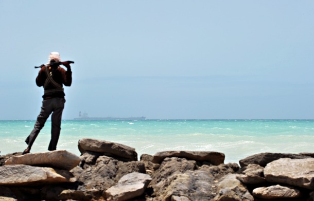 A pirate stands on a rocky outcrop on the coast in Hobyo, central Somalia, on Aug. 20, 2010. A hijacked Korean supertanker is anchored on the horizon.