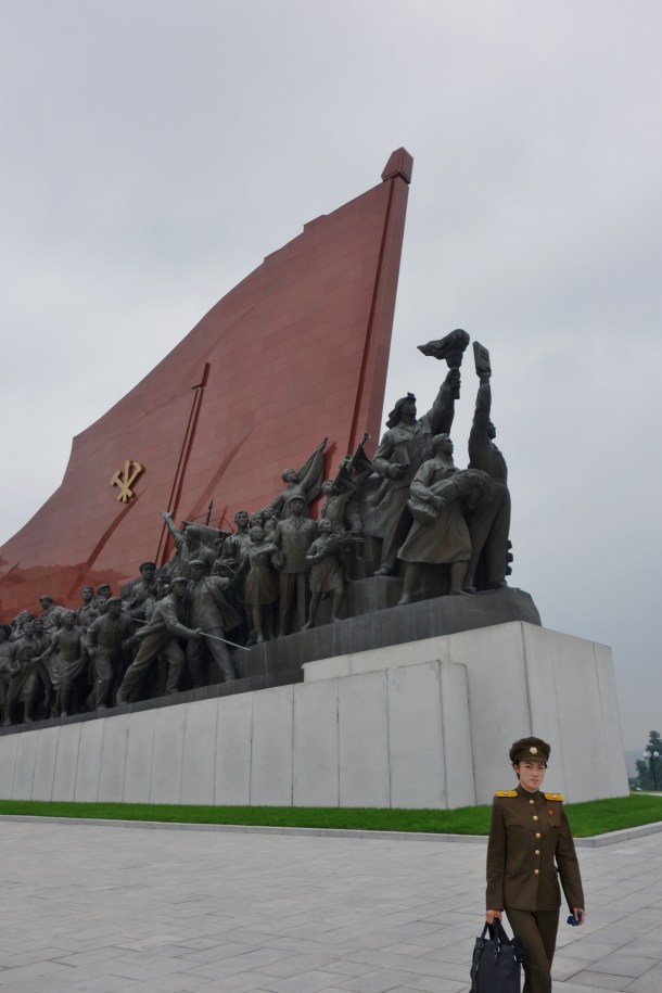 A female soldier walks past a militaristic statue in downtown Pyongyang
